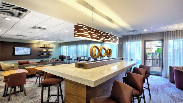En moderne hotellobby med et centralt barområde, siddepladser og et tv-skærm.