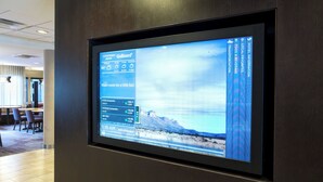 En digital skærm i et hotellobby med vejrudsigt, aktiekurser og et naturskønt bjerglandskab.