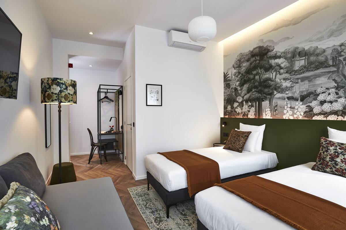 Habitación de hotel con dos camas, un escritorio y una silla. Hay un cuadro en la pared y una lámpara colgante.