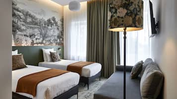 A hotel room with two beds, a sofa, a large wall mural, and a TV mounted on the wall.