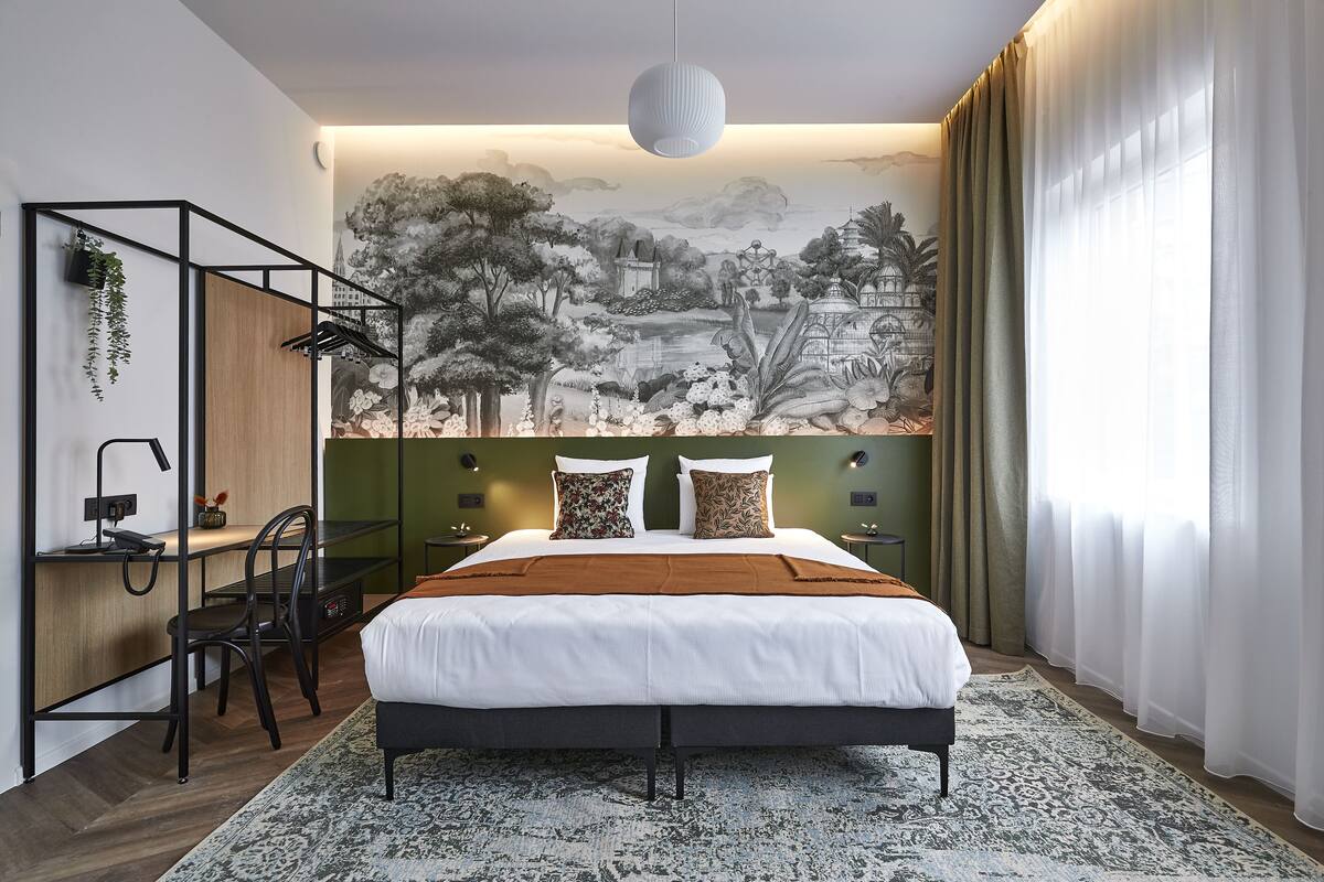 Una habitación de hotel moderna con una cama grande, un escritorio y una silla. En la pared hay un mural que representa un paisaje.