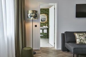 Un interior moderno con un sofá, una lámpara, un espejo y vistas a un baño con azulejos verdes.
