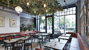 A restaurant with indoor seating, large windows, and hanging plants. - Urban Yard (Brussels)