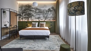 A modern bedroom with a large bed, a desk with a chair, a standing lamp, and a mural on the wall. - Urban Yard (Brussels)