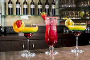 Tre cocktails på en bardisk med flasker i baggrunden.