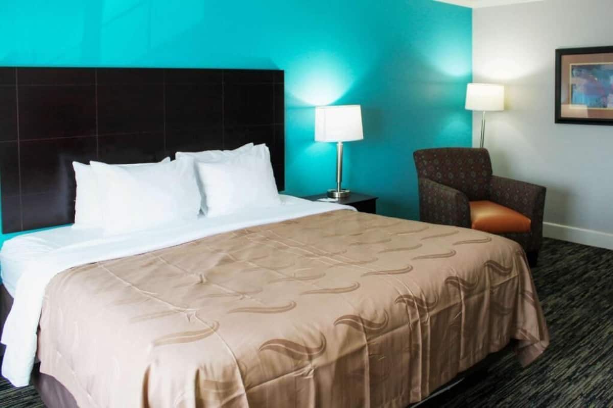 Une chambre d’hôtel avec un grand lit, une chaise, une table de chevet et une lampe.