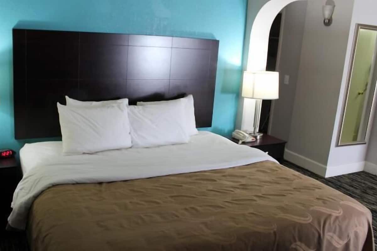 Une chambre d’hôtel avec un grand lit, deux lampes de chevet, une table de chevet, une horloge et une porte.