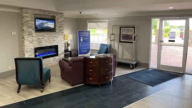 A reception area with a stone fireplace, a flat-screen TV, a blue armchair, a wooden cabinet, and a signboard. - Quality Inn Crossville Near Cumberland Mountain State Park (Crossville)