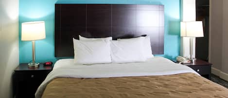 A hotel room with a bed, two bedside tables, a nightstand, a headboard, and two lamps.