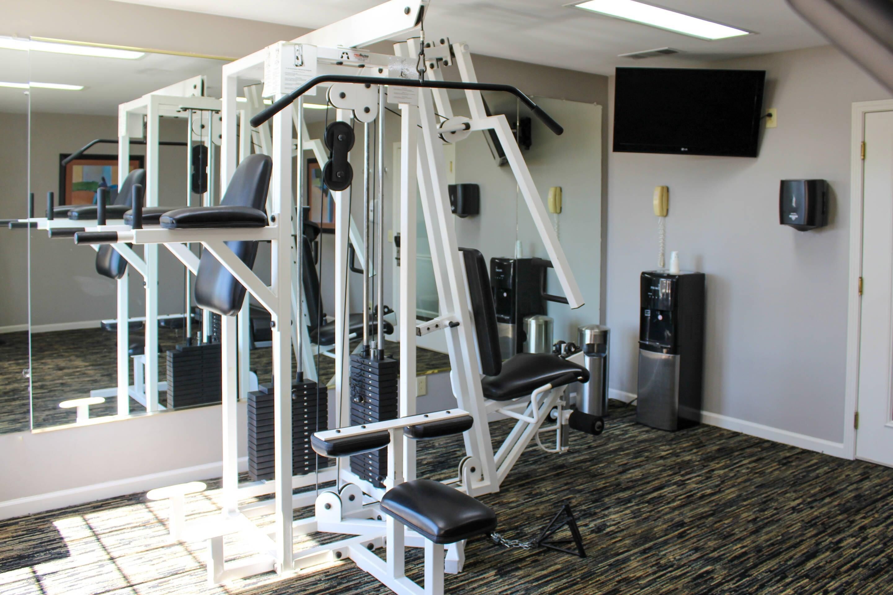 A gym with various exercise machines, a water dispenser, and a television on the wall.