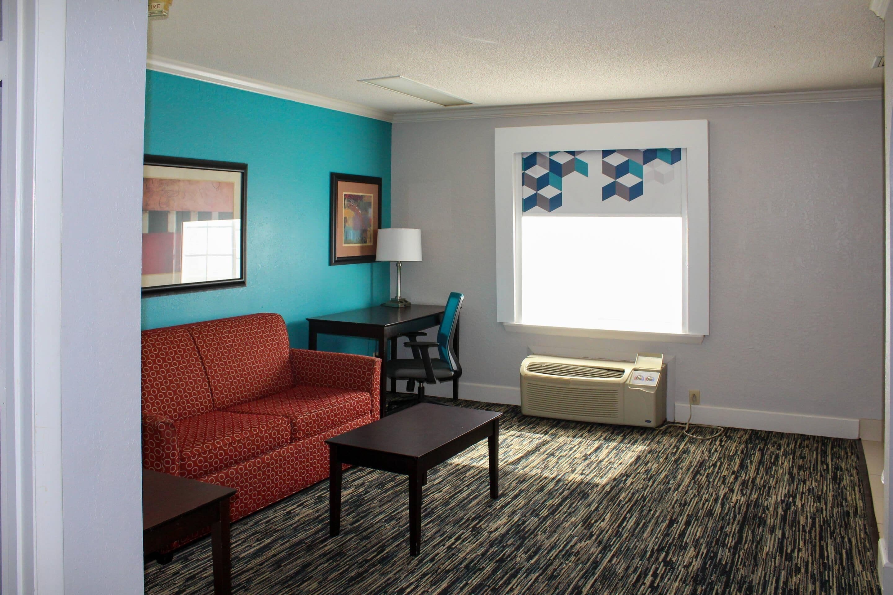 A living room with a red patterned sofa, a small table, a lamp, and a window with a geometric curtain.