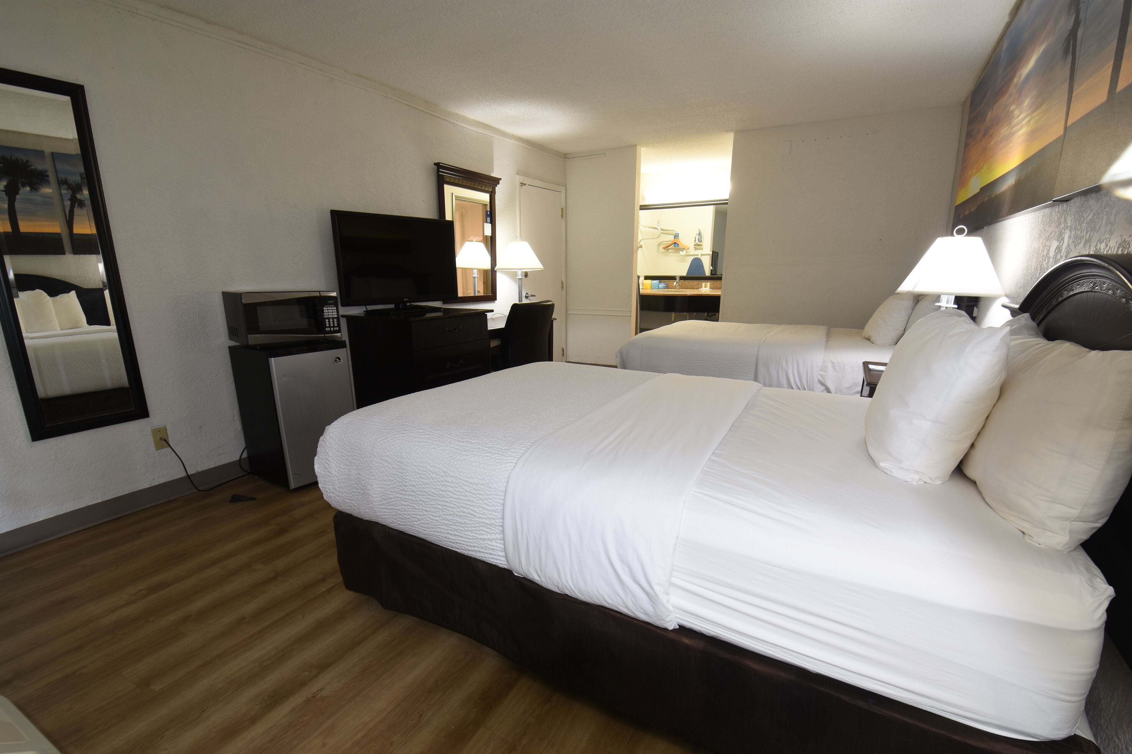 Habitación de hotel con una cama grande, un escritorio con televisor, un espejo y un cuadro en la pared.