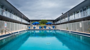 A swimming pool with blue umbrellas, a metal fence, and a building with multiple balconies.
