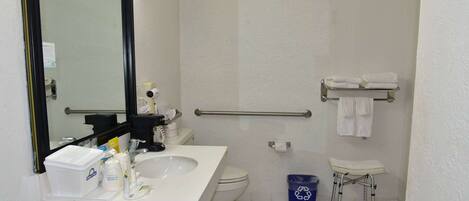 A bathroom with a white sink, toilet, and shower area. There is a mirror, a towel rack, and a grab bar.