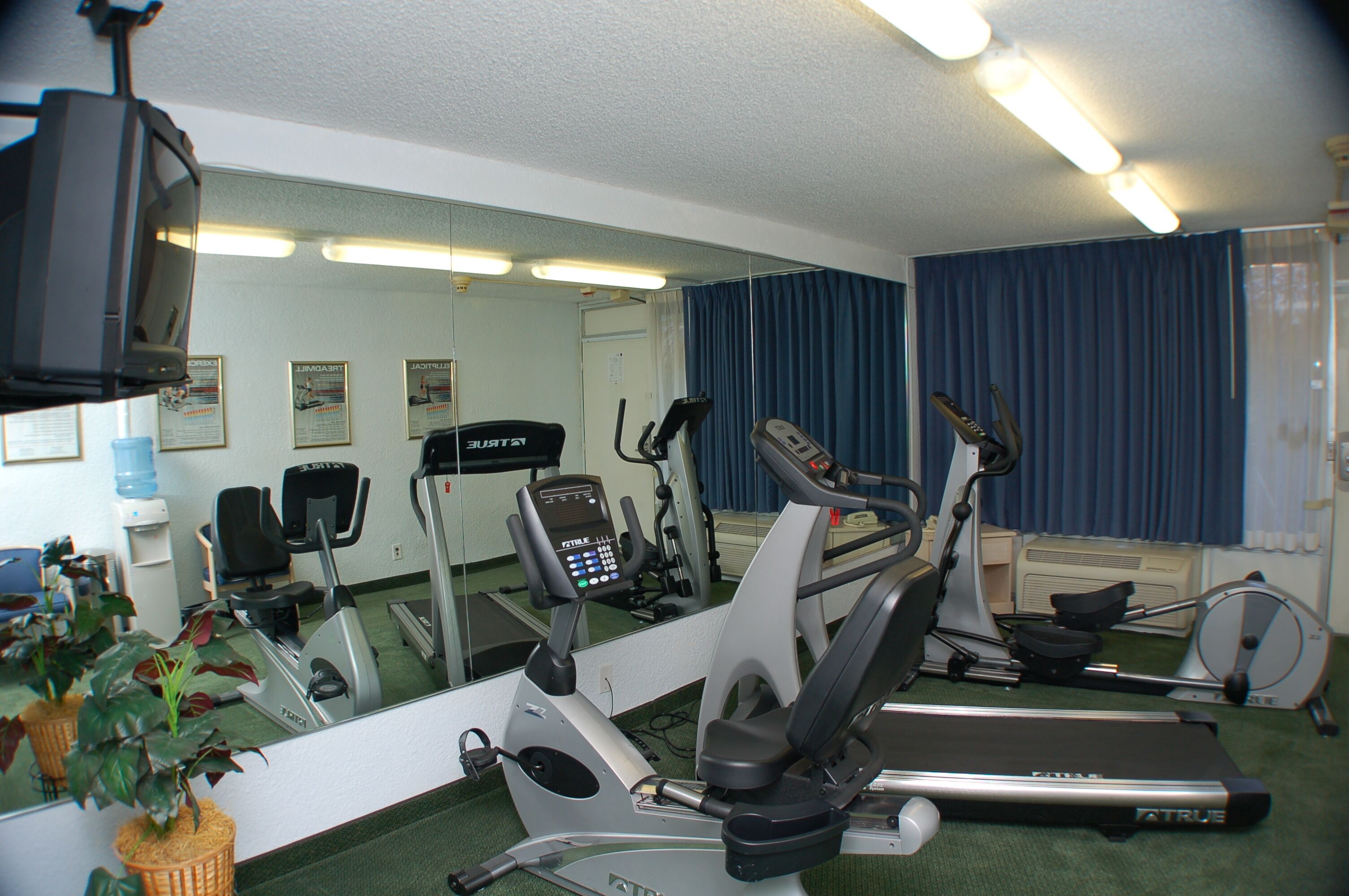 A gym with various exercise equipment, a water dispenser, and a mirror reflecting the room.