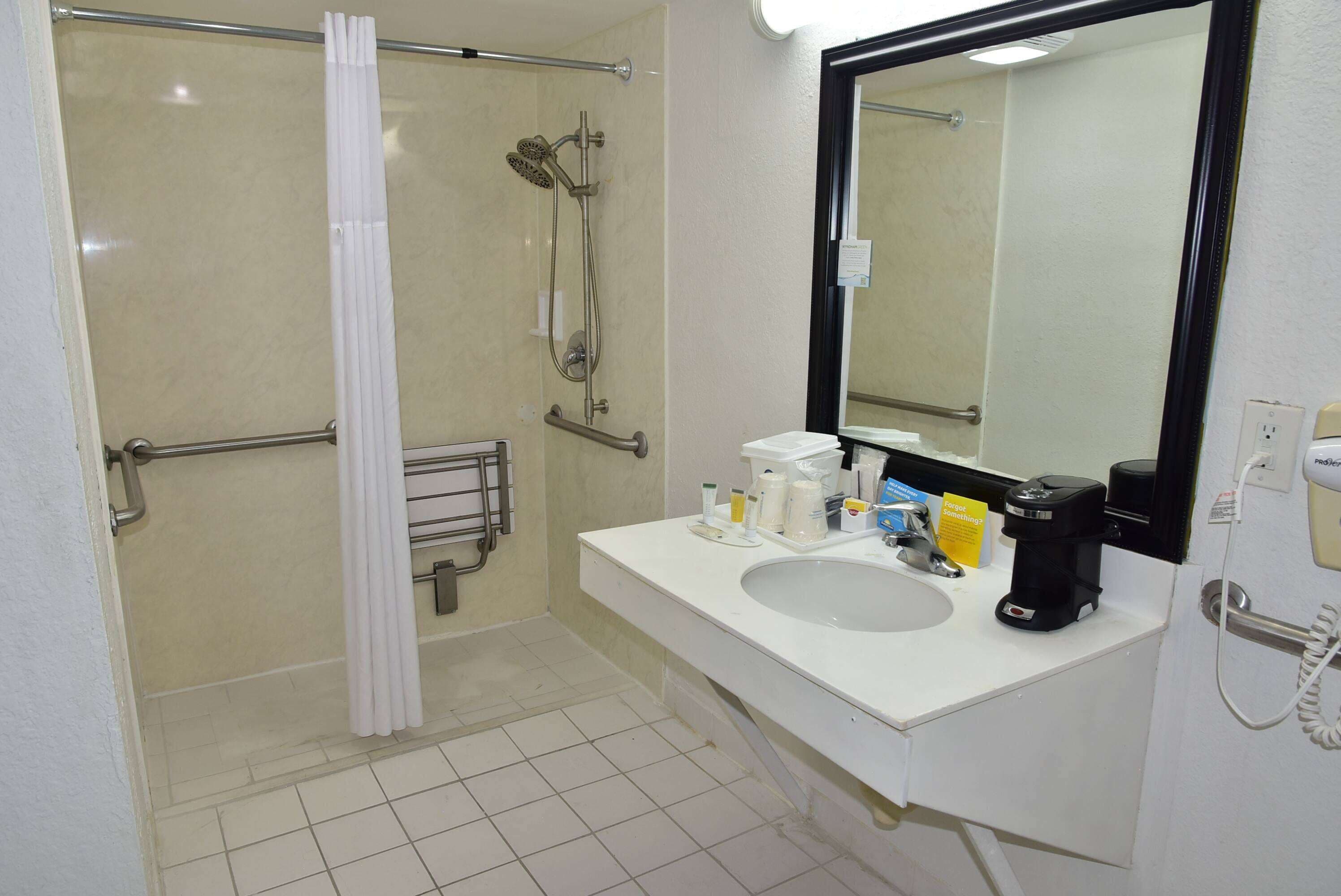 A bathroom with a shower, a sink, a mirror, and a coffee maker.