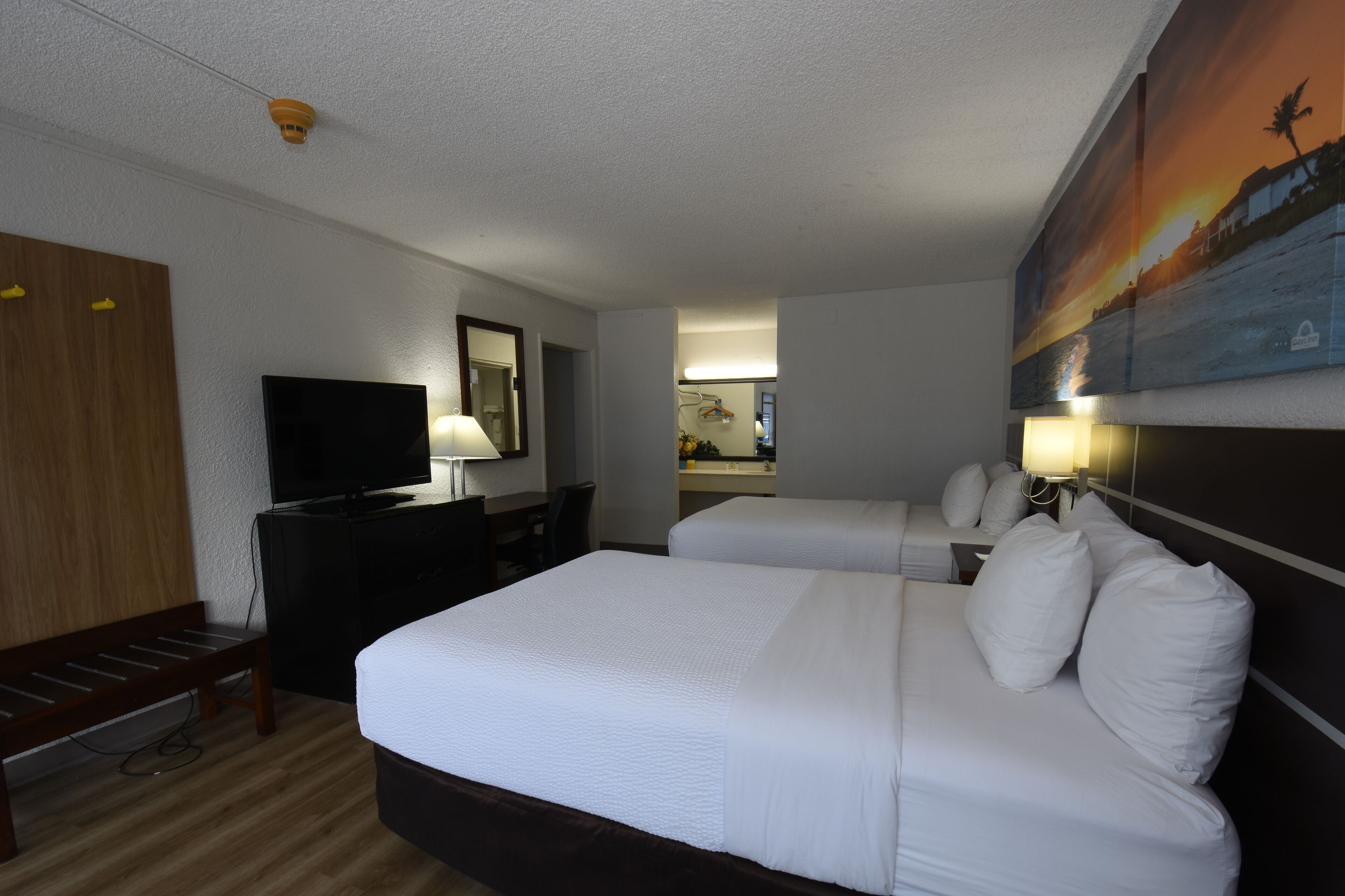 A hotel room with a large bed, a TV, a desk, and a painting on the wall.