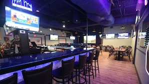 A bar area with a long counter, multiple screens, and seating arrangements.