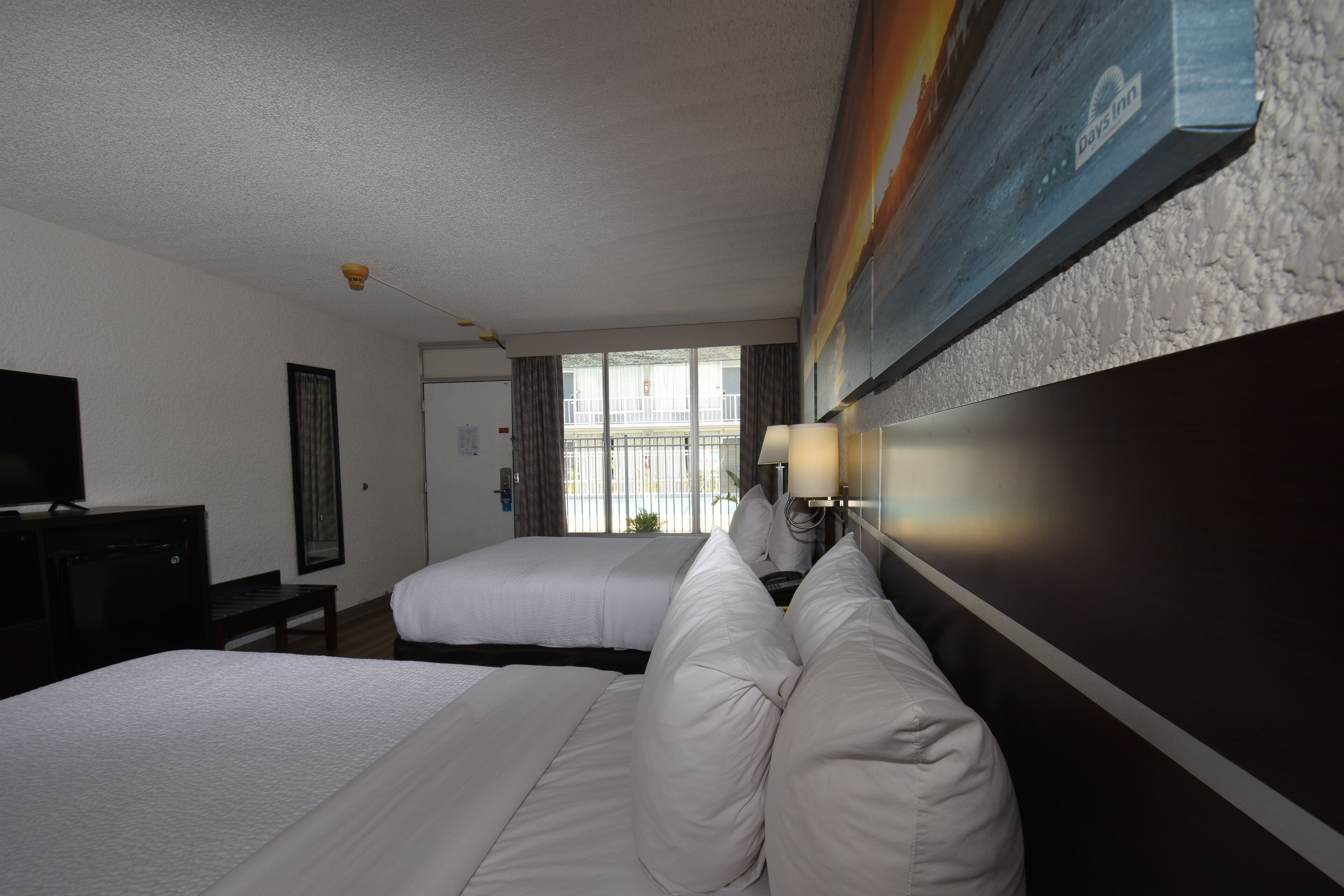 A hotel room with two beds, a TV, and a large window with curtains.
