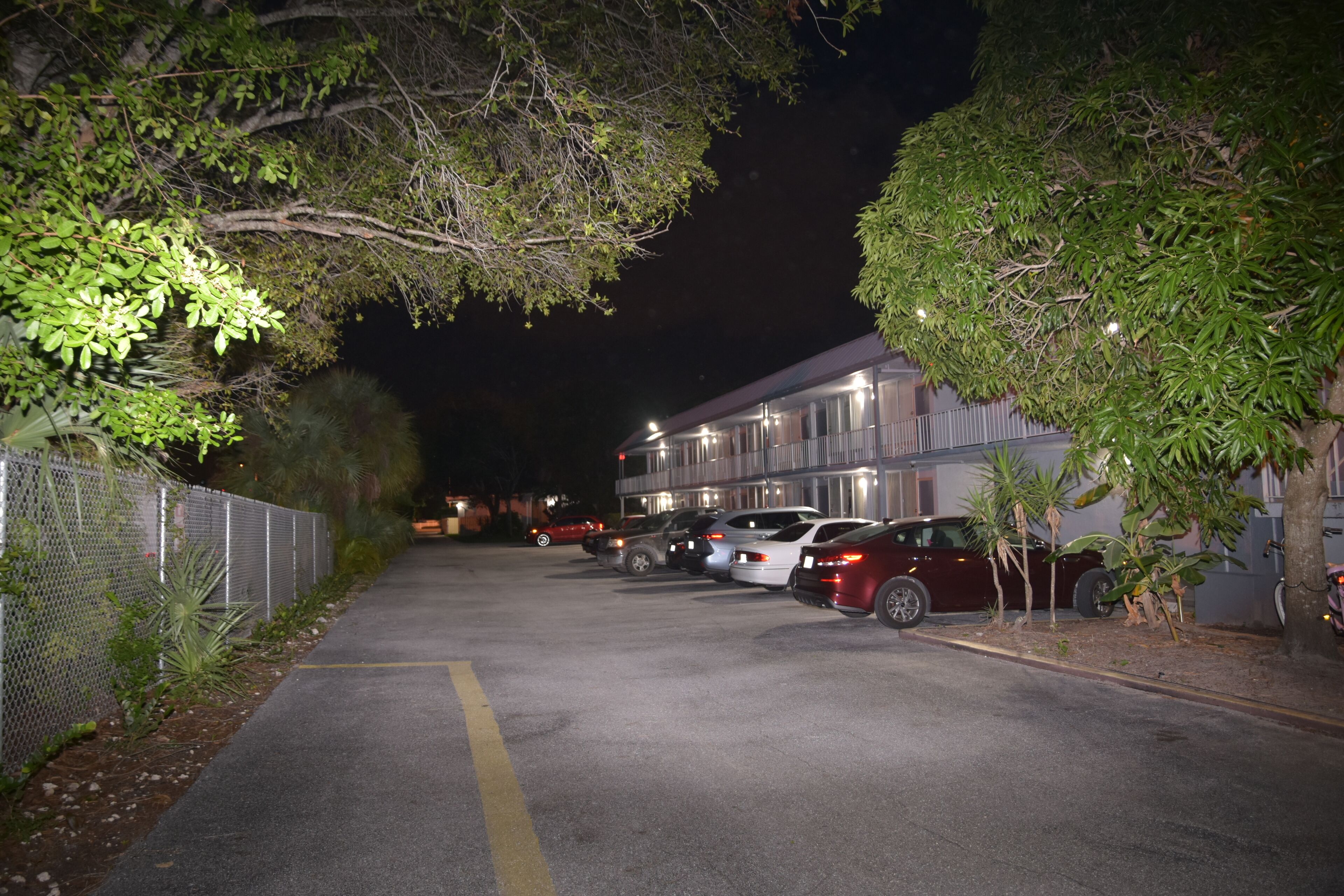 A parking lot with several cars parked in front of a building at night.