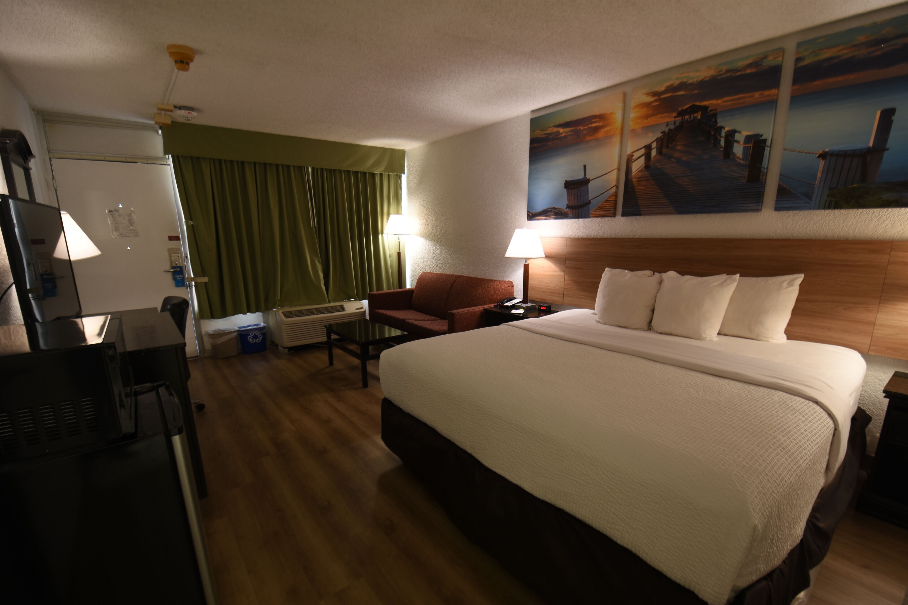 A hotel room with a large bed, a desk, a chair, a television, and a painting on the wall.