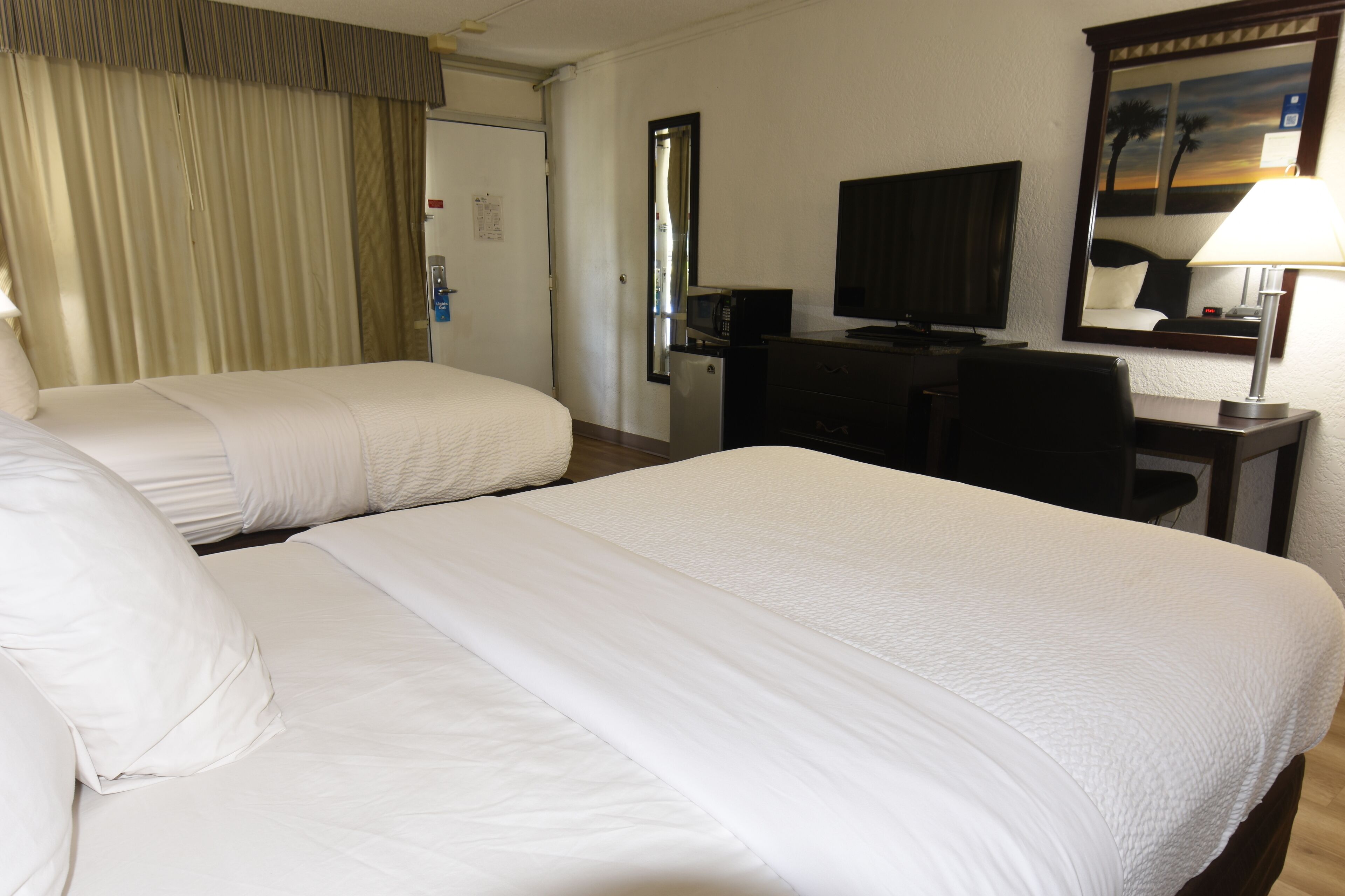 A hotel room with two beds, a desk, a television, and a mirror.