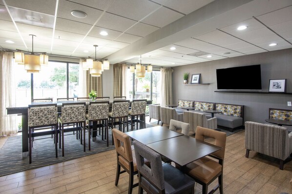 A dining area with a long table and chairs, a sofa, and a TV mounted on the wall.