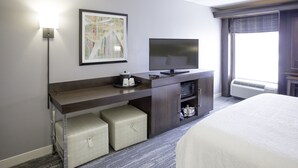 Une chambre d’hôtel avec un lit, un téléviseur posé sur une console en bois, un tableau encadré au mur et une fenêtre avec des rideaux.