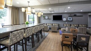 Un hall d’hôtel moderne avec un long bar, un espace salon et un téléviseur à écran plat fixé au mur.