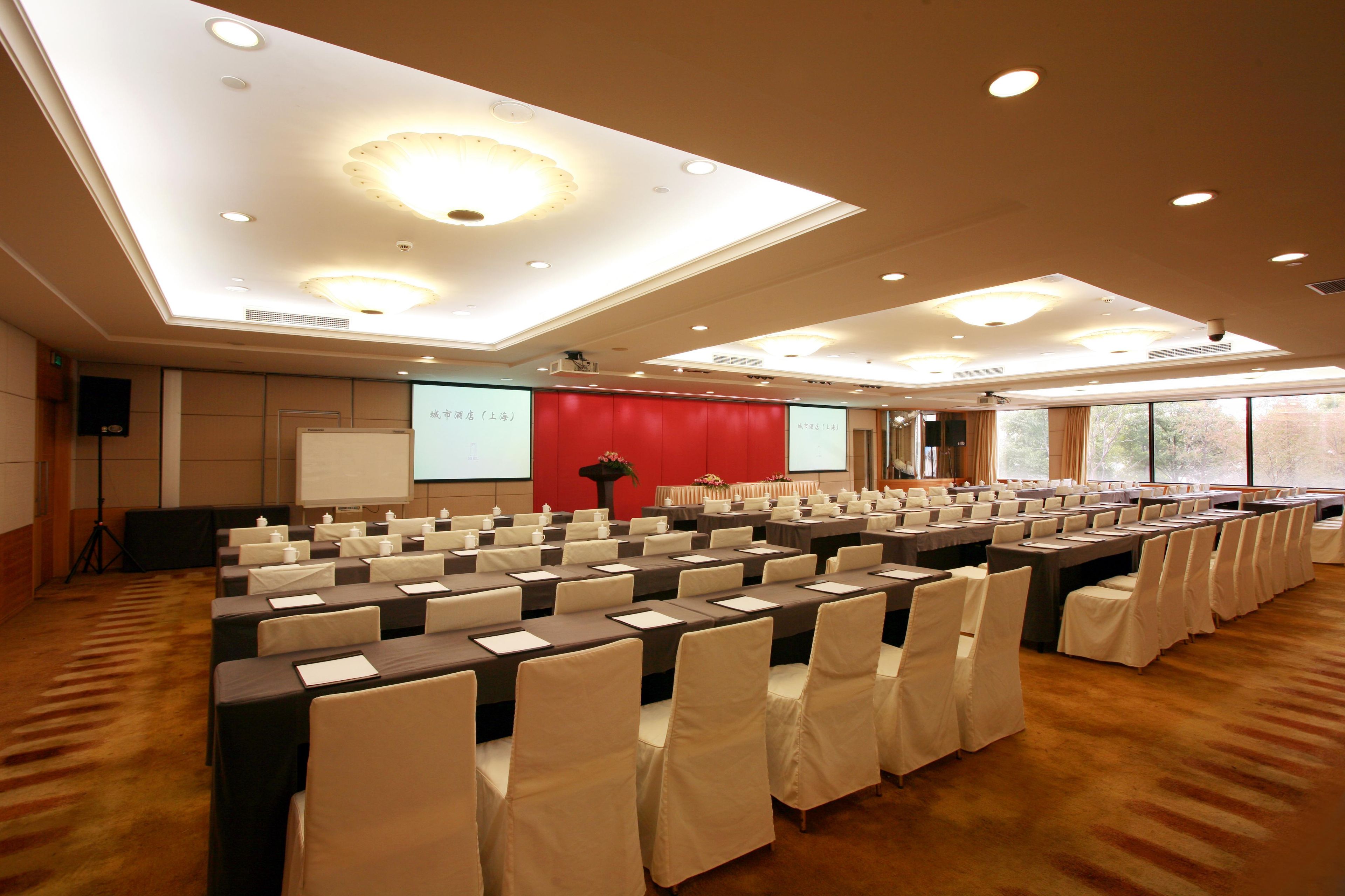 A conference room with rows of tables and chairs, a projector screen, and a red accent wall.
