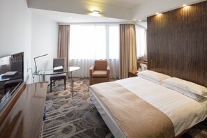 Ein Hotelzimmer mit einem großen Bett, einem Schreibtisch mit Stuhl, einem Fernseher und Blick ins Freie.