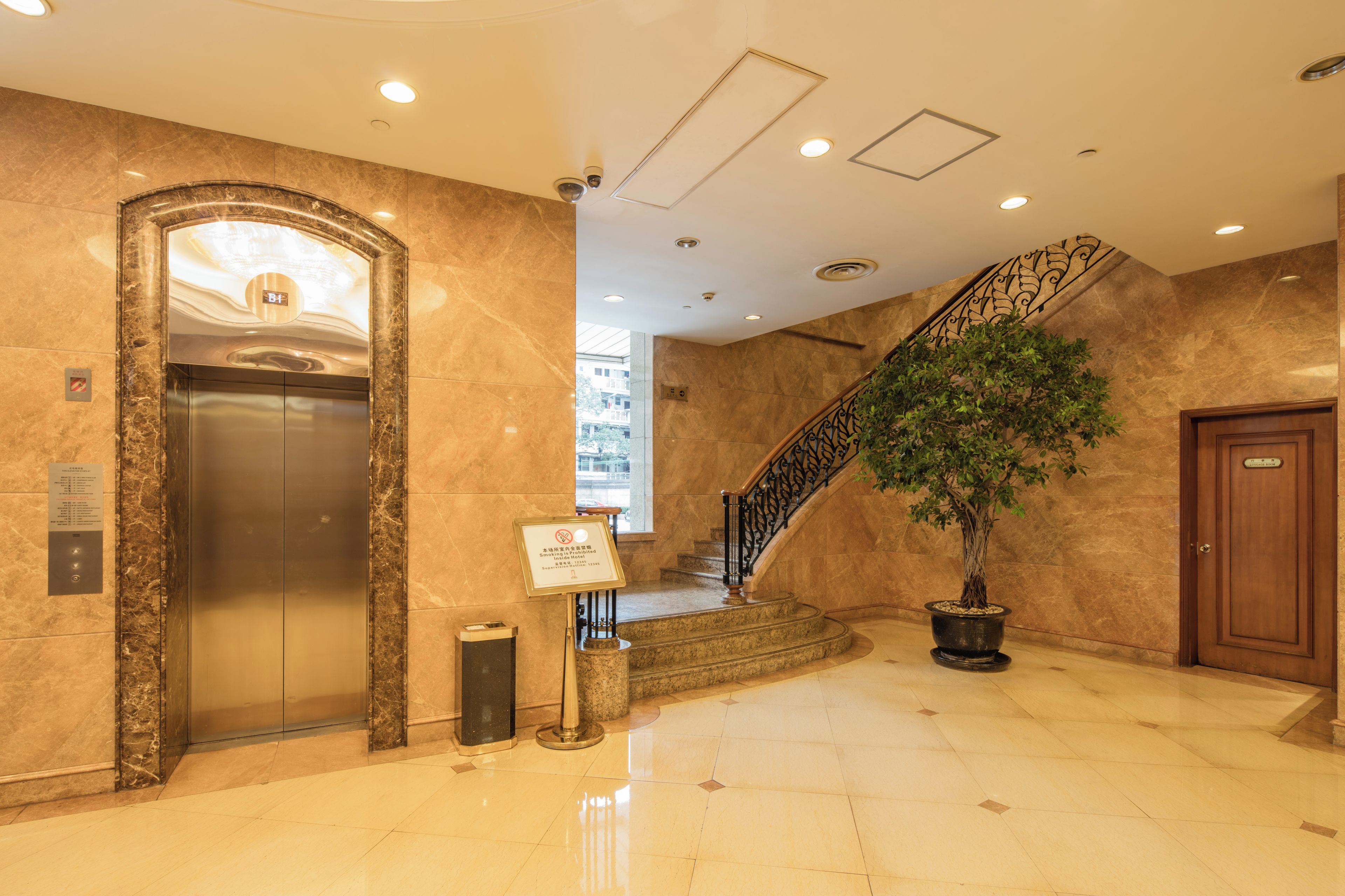 A lobby with a marble floor, an elevator, a staircase with a railing, and a potted plant.