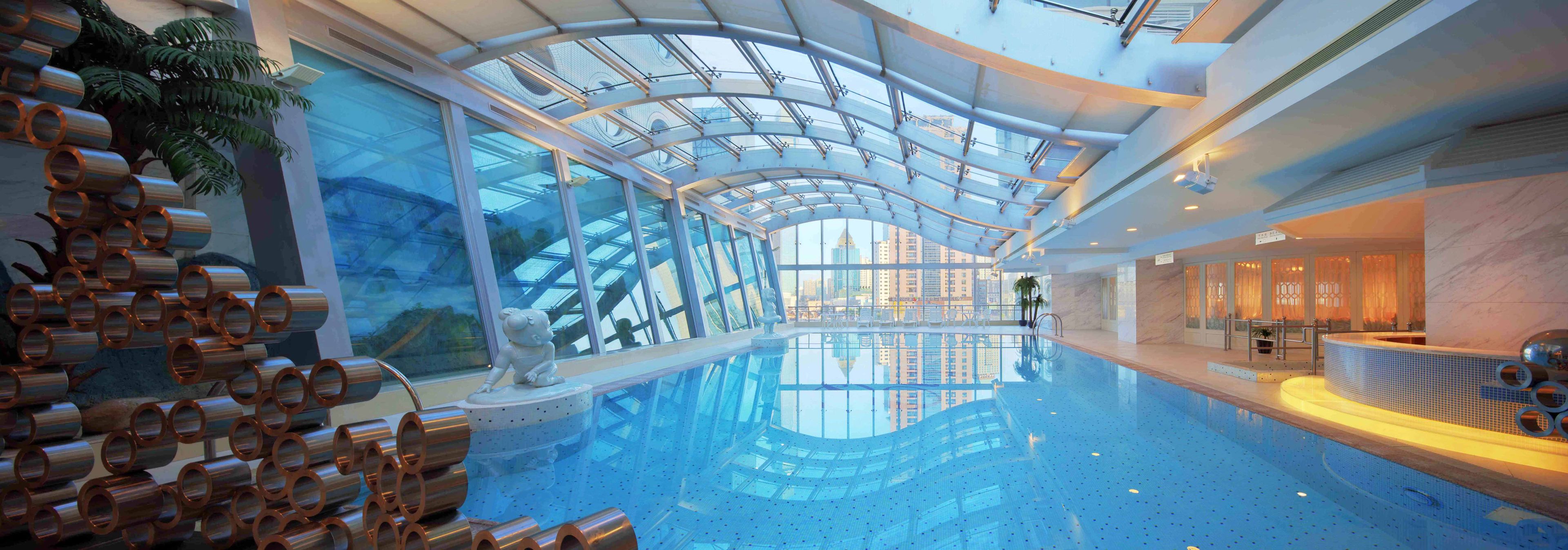 Une piscine intérieure dotée d’un toit en verre qui reflète le paysage urbain.