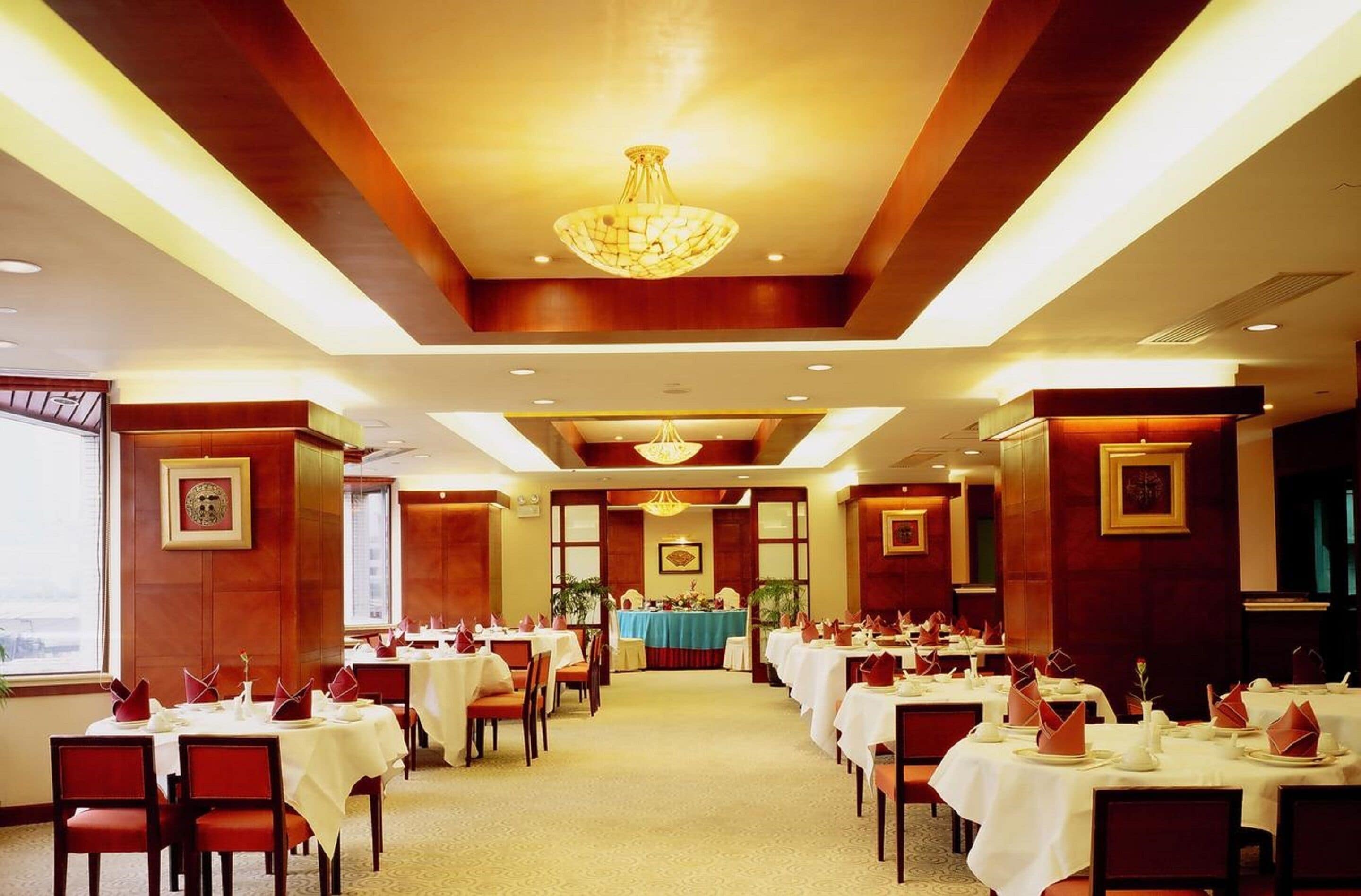 A hotel dining area with multiple tables set for guests, a central table with a blue tablecloth, and a chandelier.