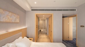 Hotellihuone, jossa on suuri sänky, yöpöytä, seinälle ripustettu taideteos ja kylpyhuone, joka näkyy avoimesta ovesta.