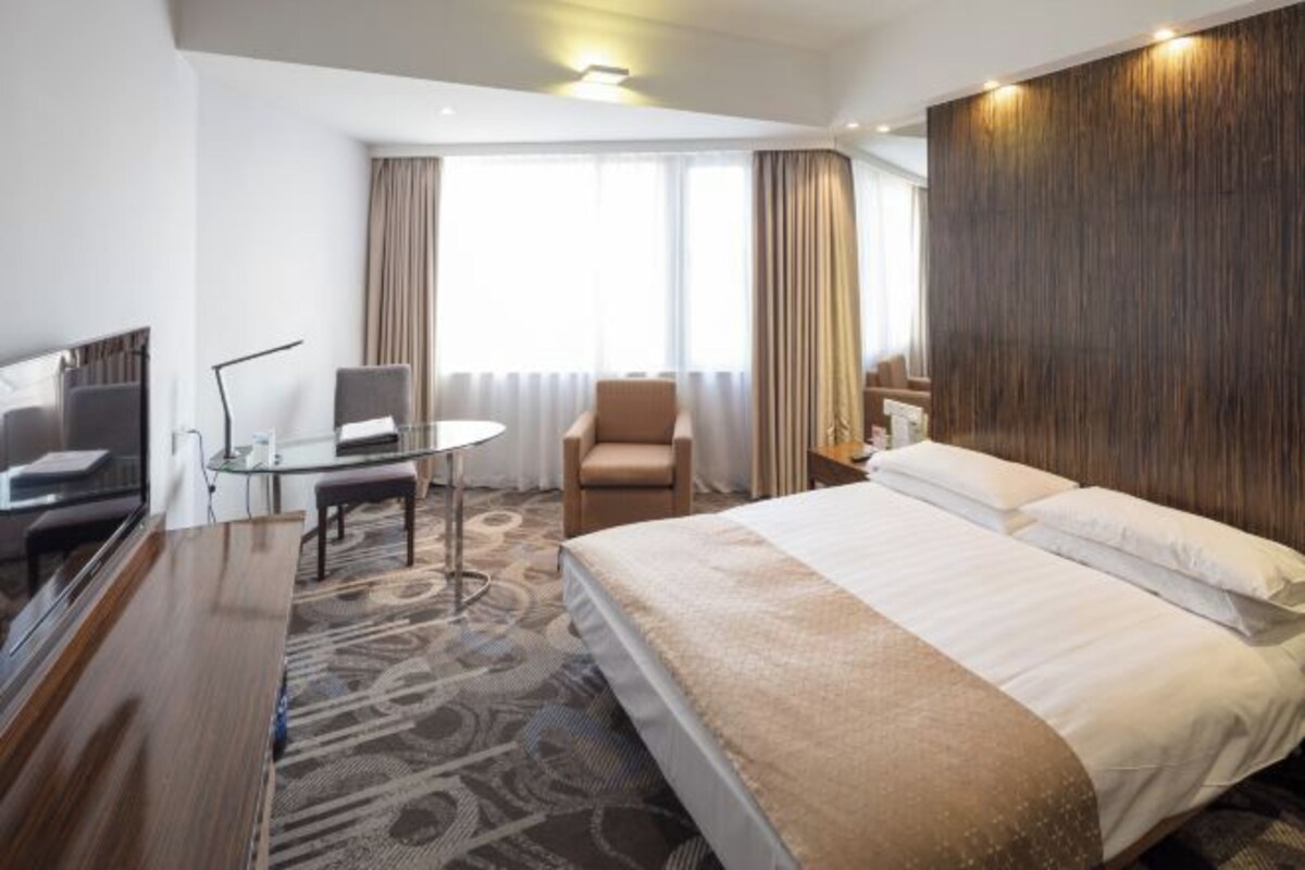 Habitación de hotel con una cama grande, un escritorio con silla, televisión y ventana con cortinas.