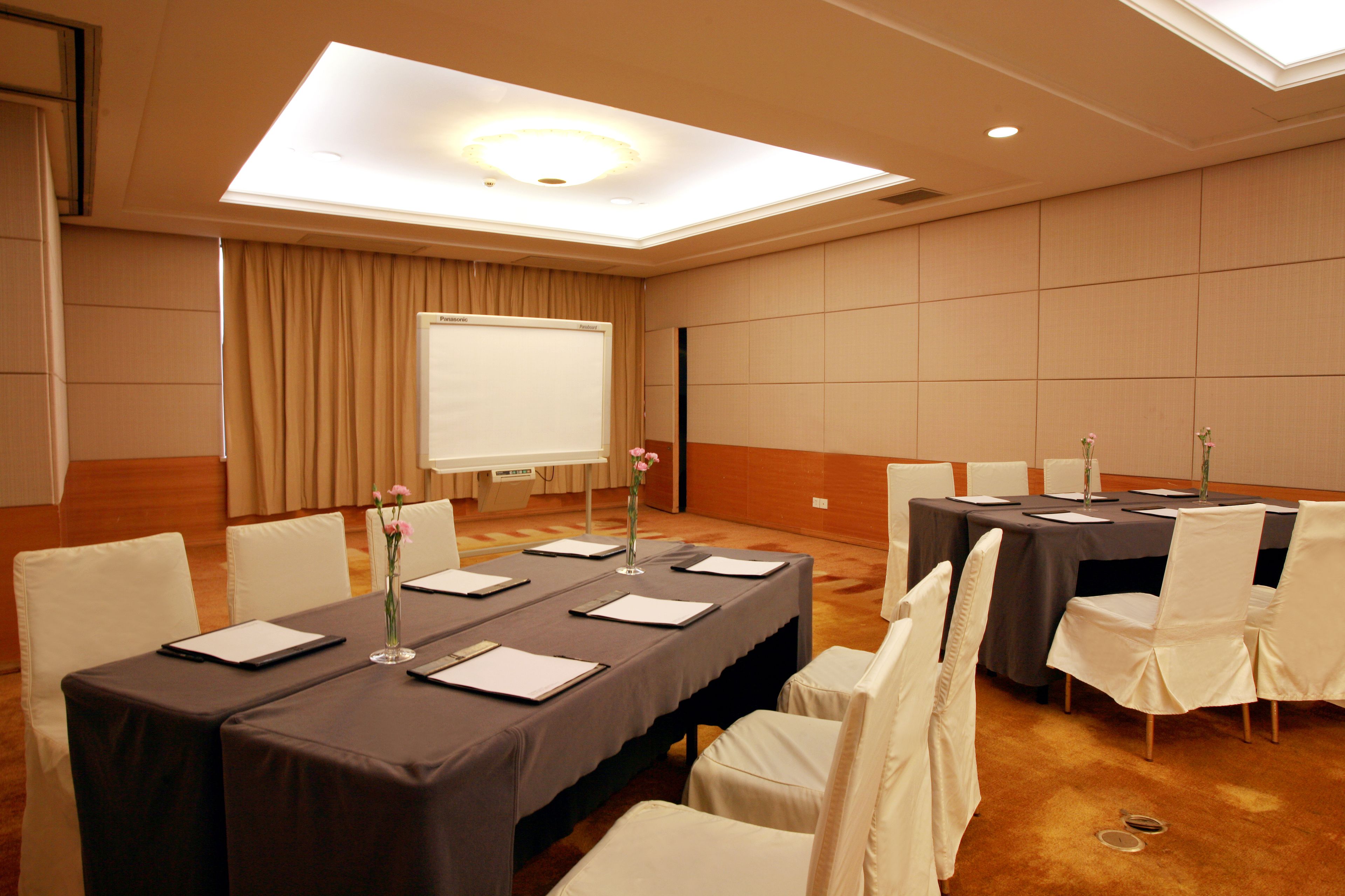 A conference room with a long table, white chairs, a projector screen, and a floral arrangement.