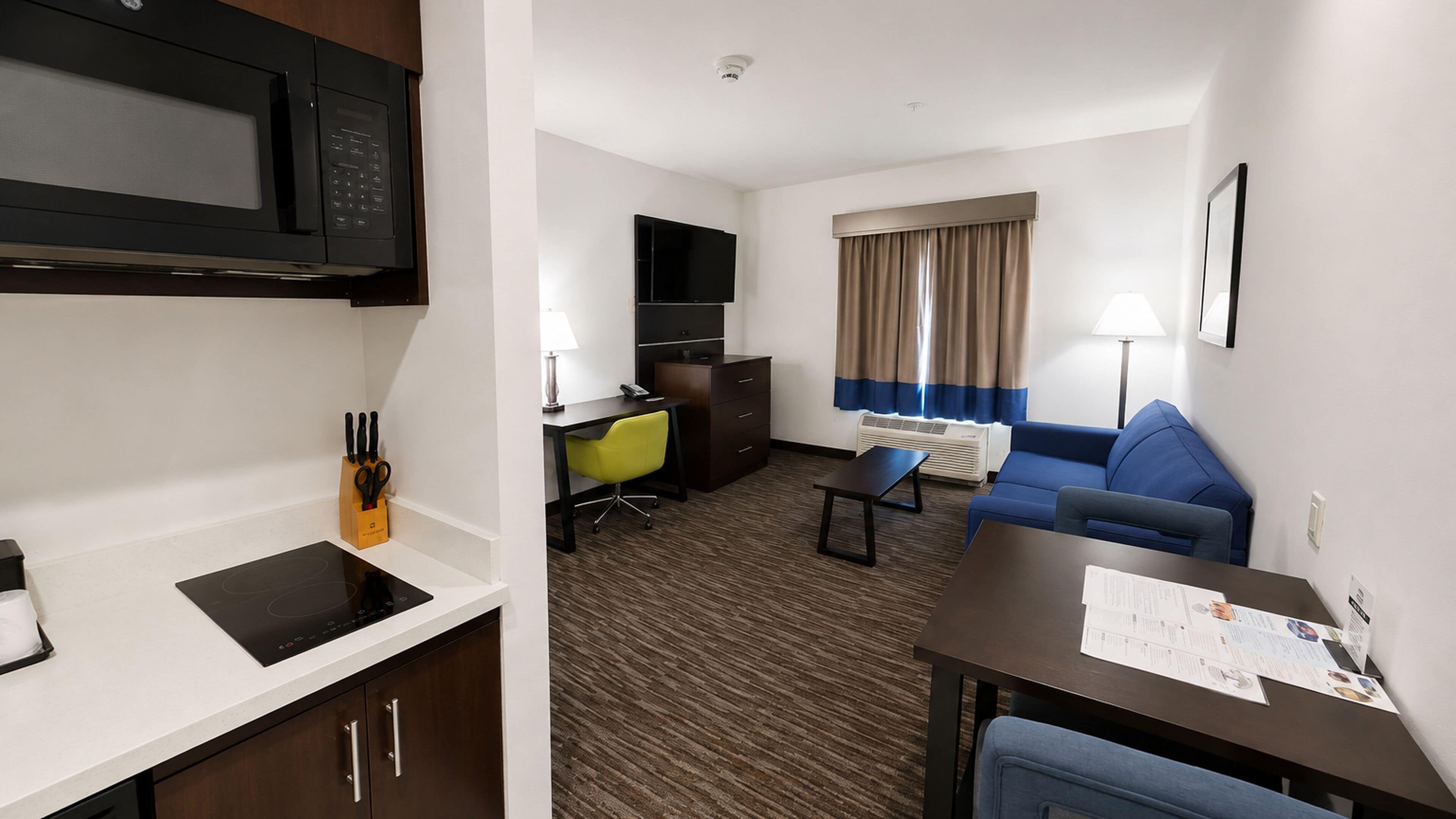 A hotel room with a kitchenette, a sofa, a desk, and a TV.