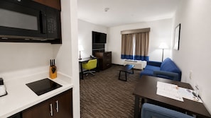 Una habitación de hotel con kitchenette, sofá, escritorio y televisión.