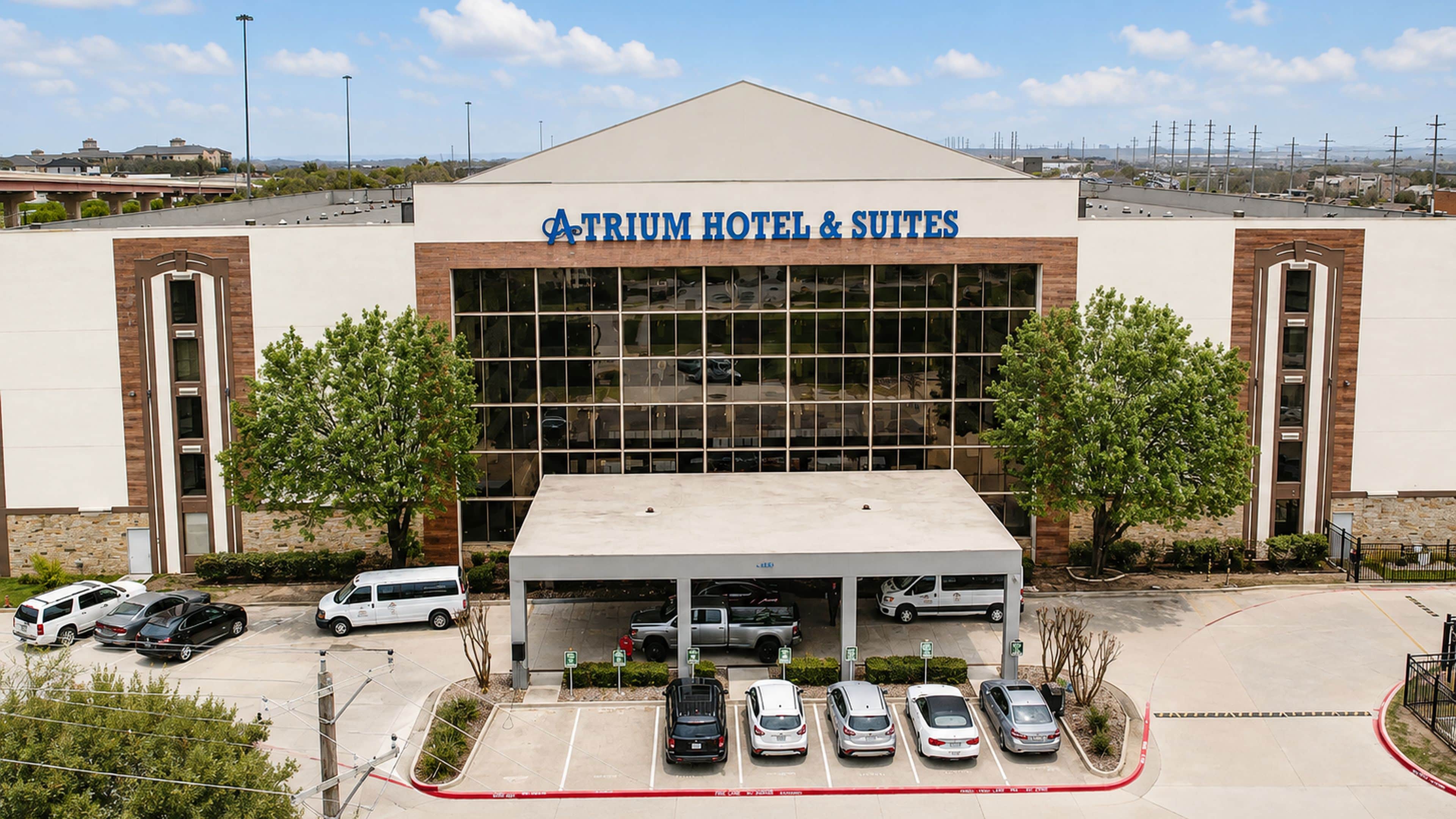 Un hotel con gran fachada de vidrio, estacionamiento techado y cielo despejado.