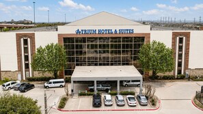Un hotel con gran fachada de vidrio, estacionamiento techado y cielo despejado.