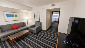 Habitación de hotel con sofá, sillón, televisión y lámpara.
