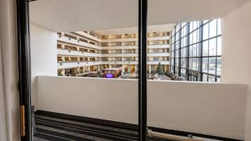 Un vestíbulo de hotel de varios niveles con un área de estar central, un árbol de Navidad y vista al estacionamiento a través de grandes ventanales.
