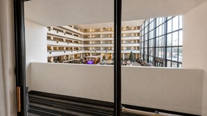 Un vestíbulo de hotel de varios niveles con un área de estar central, un árbol de Navidad y vista al estacionamiento a través de grandes ventanales.