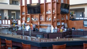 Zona de bar con mostrador, taburetes y estanterías llenas de botellas y vasos.