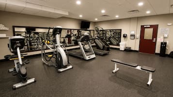 A gym with various exercise equipment, a bench, and a door with an emergency exit sign.