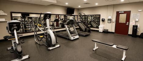 A gym with various exercise equipment, a bench, and a door with an emergency exit sign.