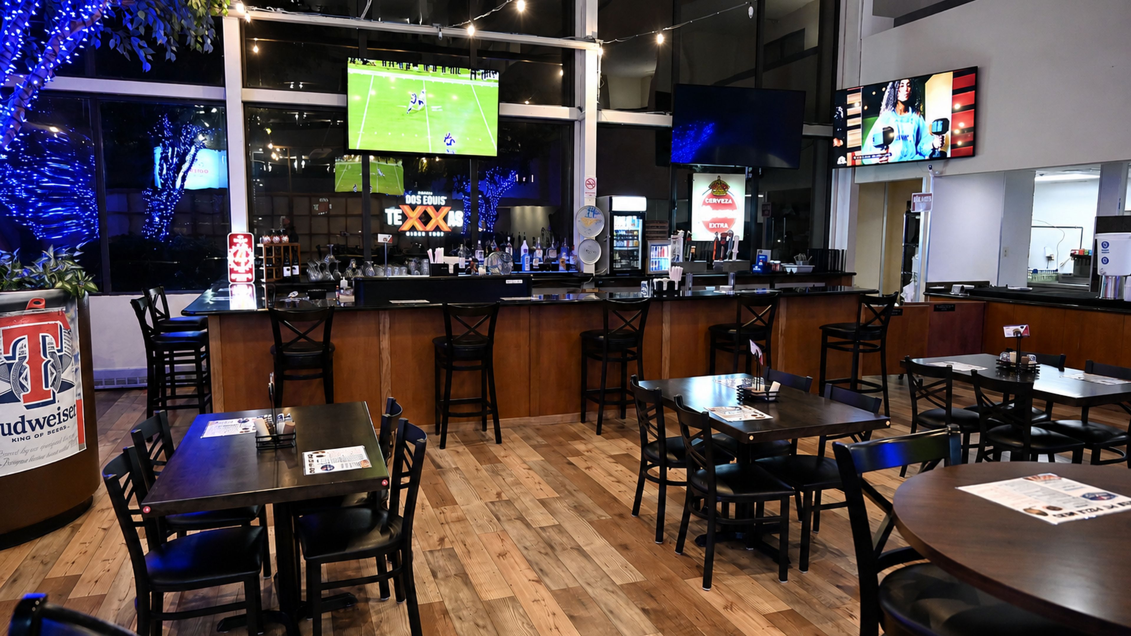A bar area with multiple seating options, a counter with various bottles, and a television displaying a sports game.