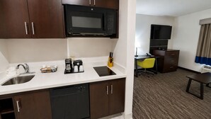 Une chambre d’hôtel équipée d’une kitchenette comprenant un four à micro-ondes, une machine à café et un évier. La chambre dispose également d’un bureau avec une chaise et d’une télévision.
