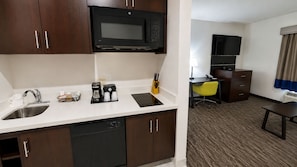Habitación de hotel con kitchenette, que incluye microondas, cafetera y fregadero. Cuenta con un escritorio, una silla y un televisor.